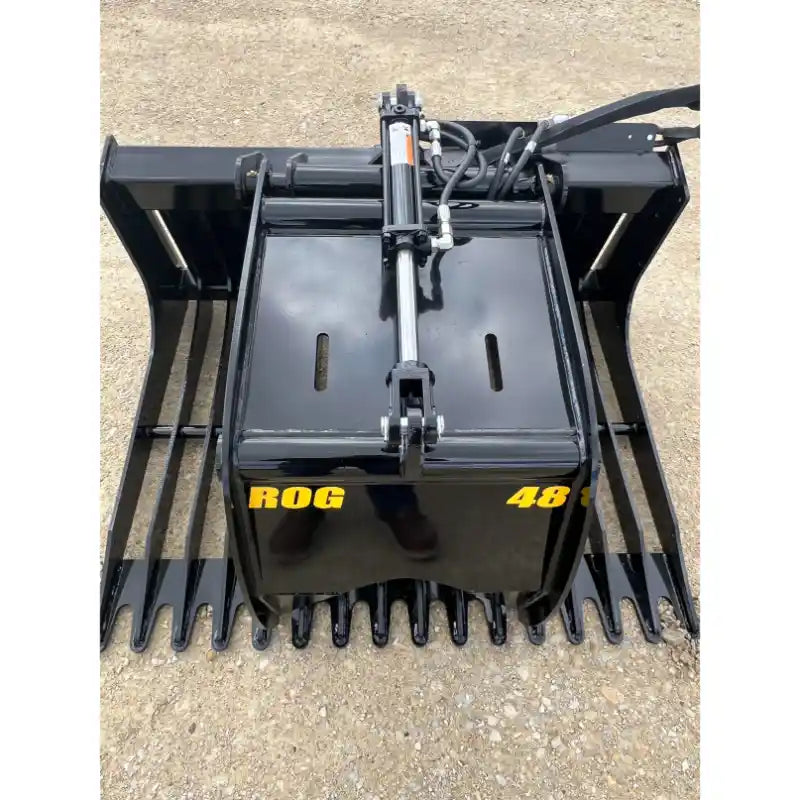 Black steel skid steer grapple attachment with wide flat curved tines, hydraulic cylinder, and hoses on gravel surface outdoors