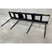 Black steel skid steer attachment with four long pointed tines on concrete floor viewed from front angle