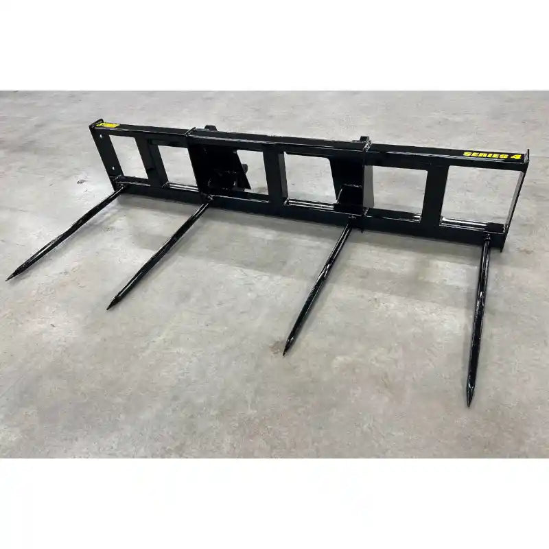 Black steel skid steer attachment with four long pointed tines on concrete floor viewed from front angle