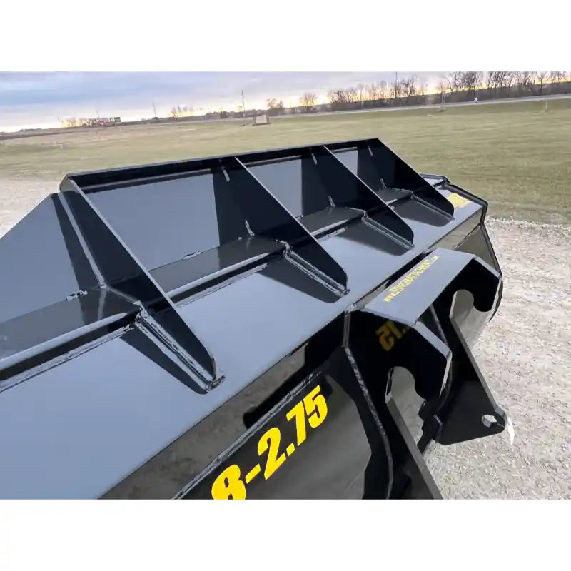 Close-up of black steel construction bucket attachment showing reinforced gussets and smooth welded edges outdoors