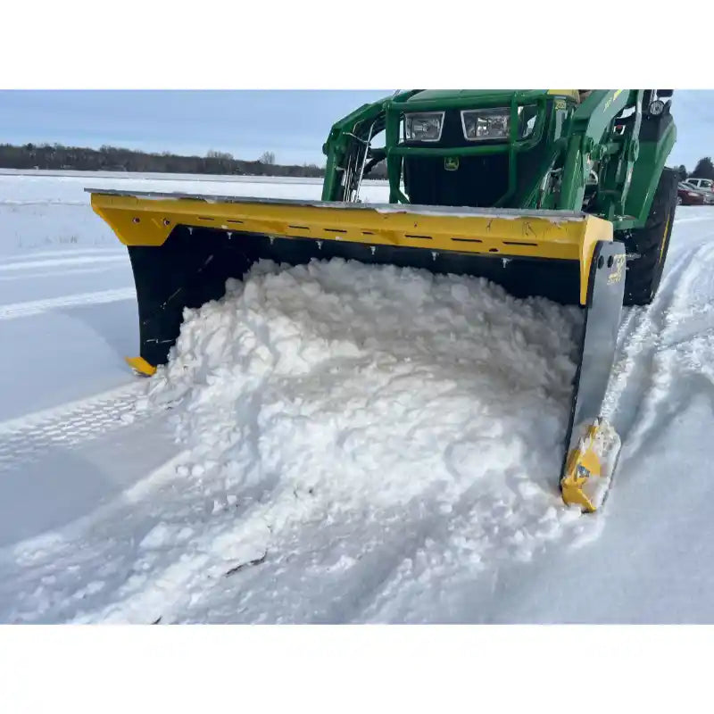 Yellow and black steel snow pusher attachment clearing packed snow mounted on green tractor on snowy field