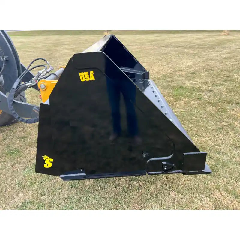Black painted hydraulic dump bucket attachment mounted on tractor loader arm with visible hoses on grass field