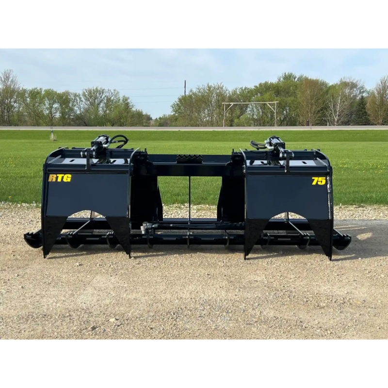 Black skid steer root grapple attachment with dual grapple arms, hydraulic cylinders, and reinforced steel frame on gravel surface
