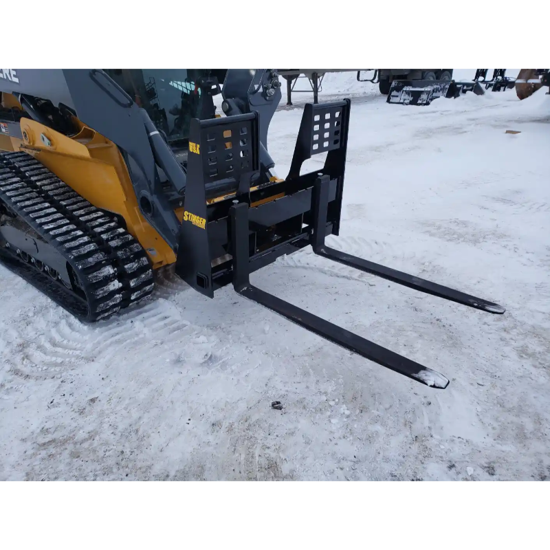 Black steel skid steer pallet fork attachment with two long tines and reinforced vertical backrest on snowy ground