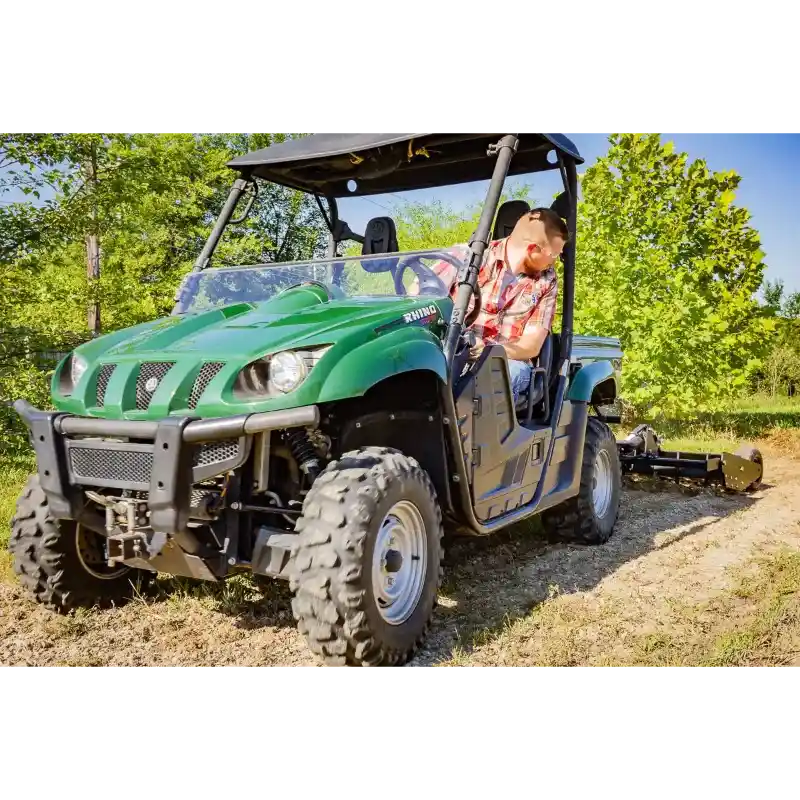 Green utility vehicle with roll cage pulling Swisher 48" Driveway Grader on dirt path, gallery position 1