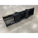 Black metal skid steer rock bucket attachment with reinforced back plates and spaced vertical tines on concrete floor
