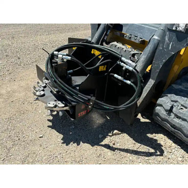 Black skid steer stump grinder attachment with hydraulic hoses, cutting teeth, and steel mounting frame on gravel surface