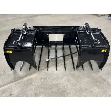 Front view of black metal manure grapple attachment with multiple curved tines and hydraulic cylinders on concrete floor