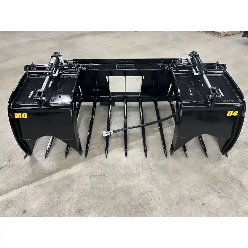 Black steel manure grapple attachment with dual hydraulic cylinders and pointed tines on concrete floor indoors