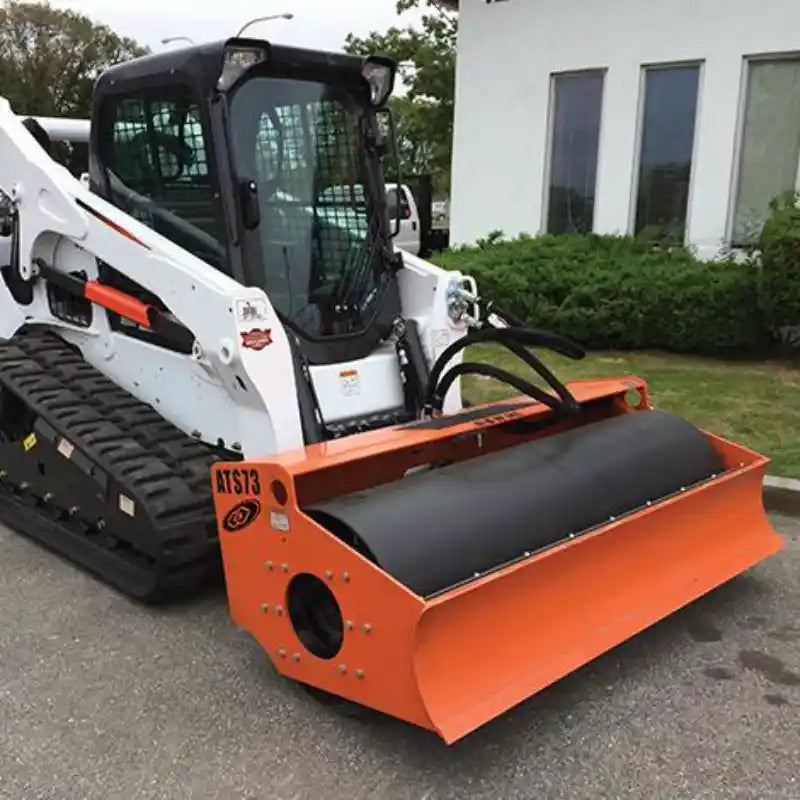 Compact white skid steer with orange smooth drum roller attachment parked on pavement near building