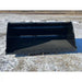 Front view of large black steel skid steer bucket attachment resting on snow-dusted ground outdoors