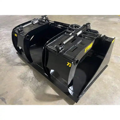 Black steel demolition grapple attachment with dual hydraulic cylinders sitting on concrete floor indoors