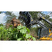 Yellow Deere skid steer with black clam grapple attachment lifting uprooted tree among dense green vegetation under blue sky