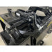 Black steel demolition grapple attachment focusing on hydraulic cylinder and hose connections indoors on concrete floor