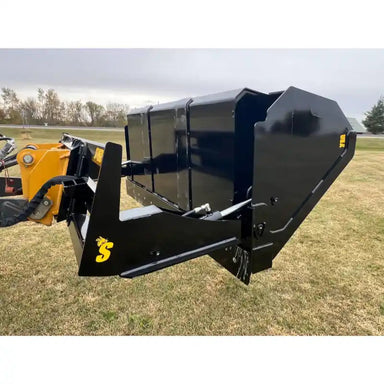 Black hydraulic dump bucket attachment with tilt-back feature mounted on yellow tractor arm over grass field