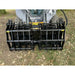 Black steel clam grapple attachment mounted on a skid steer loader parked on dirt with fallen leaves