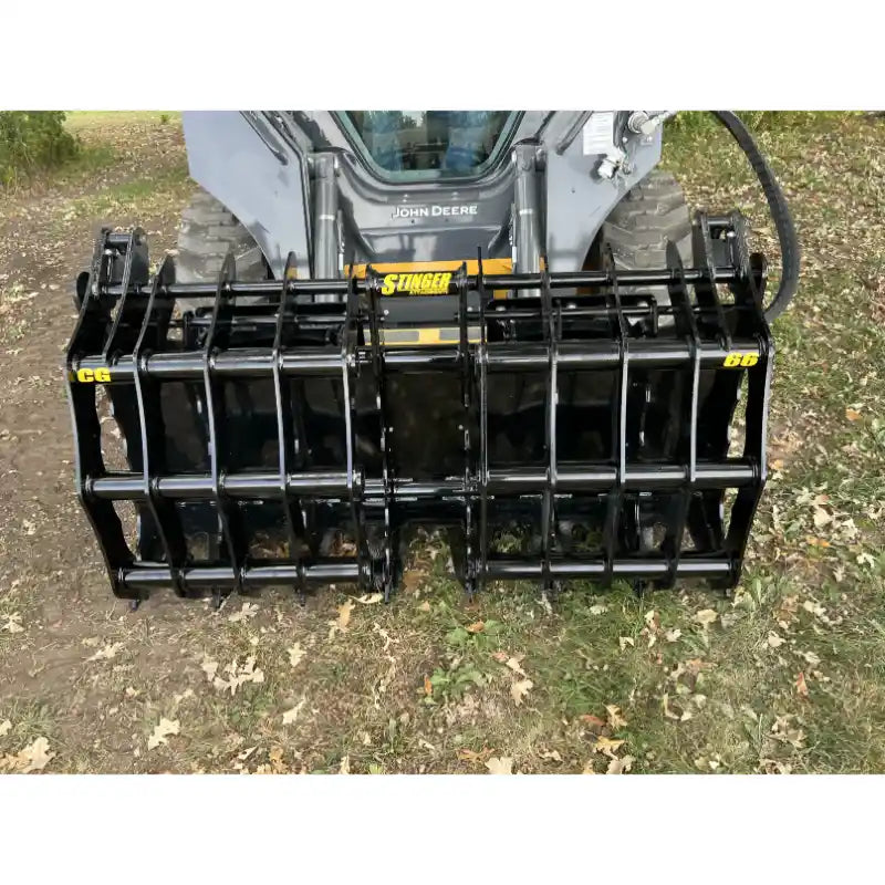 Black steel clam grapple attachment mounted on a skid steer loader parked on dirt with fallen leaves