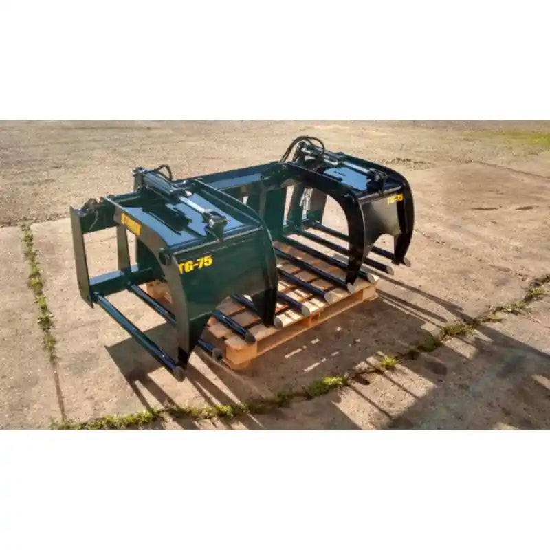 Green-painted steel skid steer grapple attachment with two hydraulic cylinders and curved tines on wooden pallet outdoors
