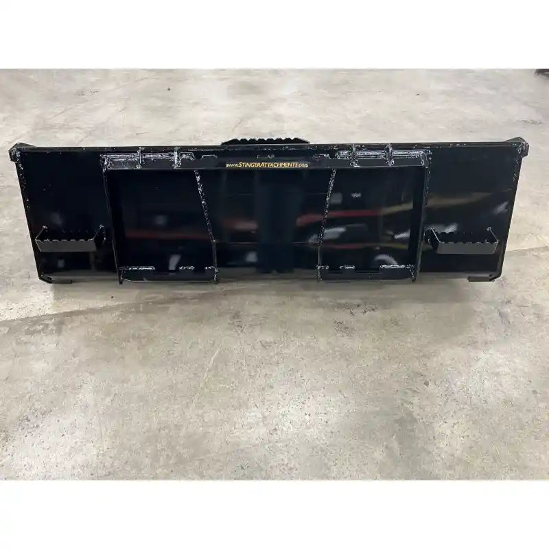 Black steel skid steer material bucket attachment with reinforced center braces and mounting brackets on concrete floor