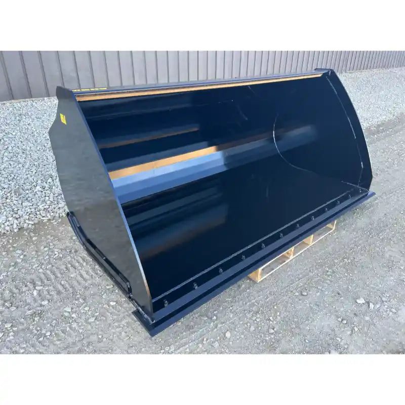 Front view of a smooth black steel skid steer material bucket with welded cutting edge on gravel surface