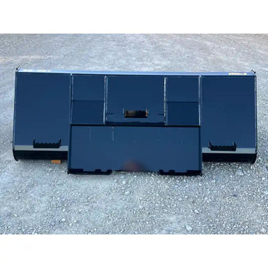 Front view of black steel tractor liquid slurry bucket attachment resting on rough gravel surface outdoors
