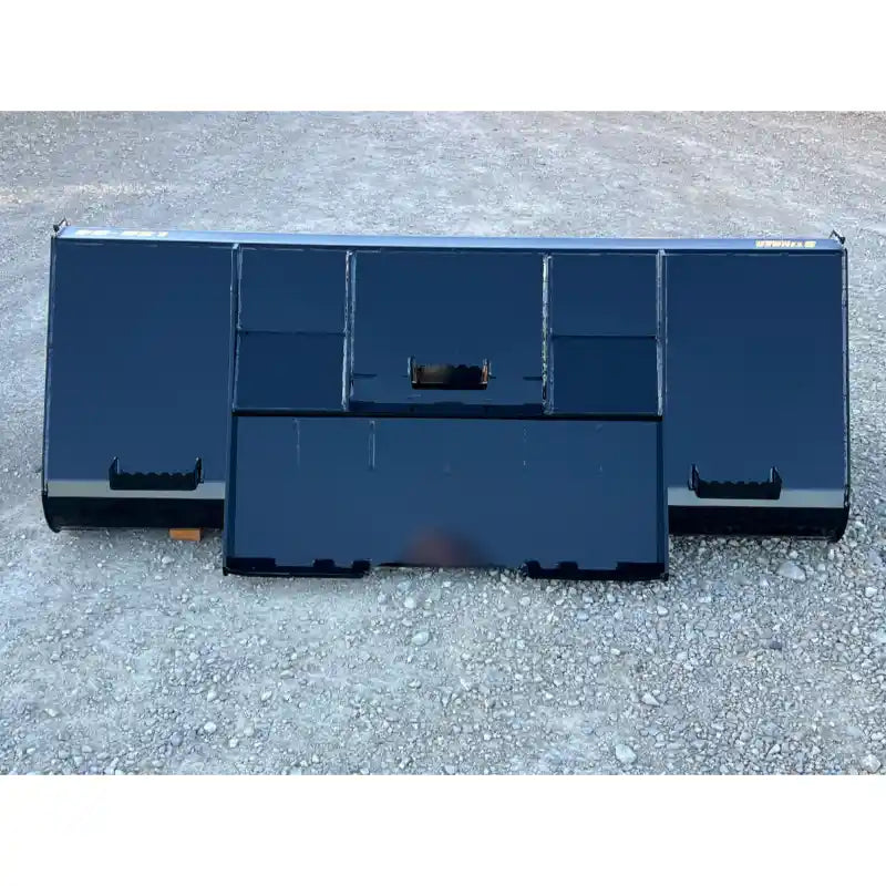 Front view of black steel tractor liquid slurry bucket attachment resting on rough gravel surface outdoors