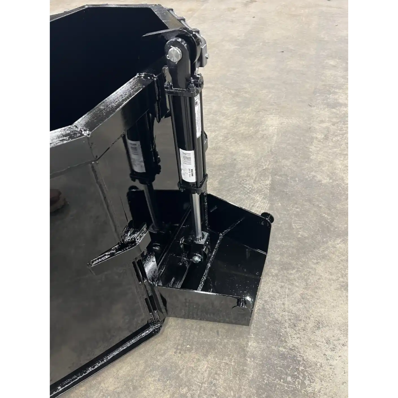 Black steel concrete bucket attachment with hydraulic dump cylinder and reinforced bottom edge on concrete floor
