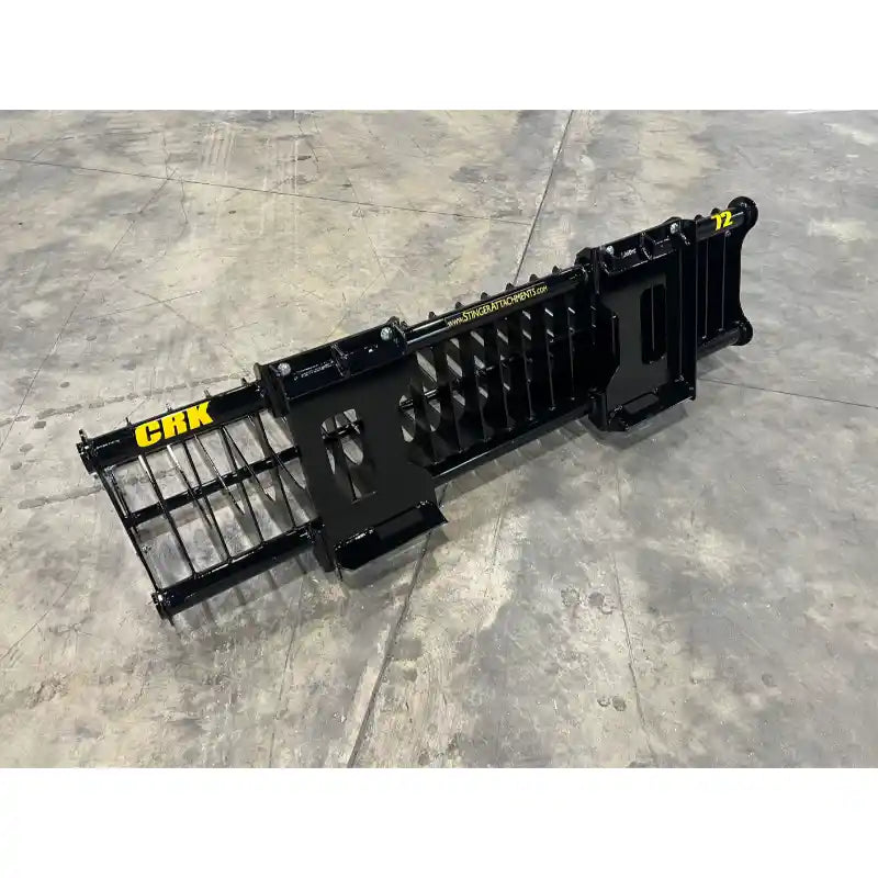 Long black metal rock bucket attachment with spaced tines and reinforced mounting brackets on concrete floor