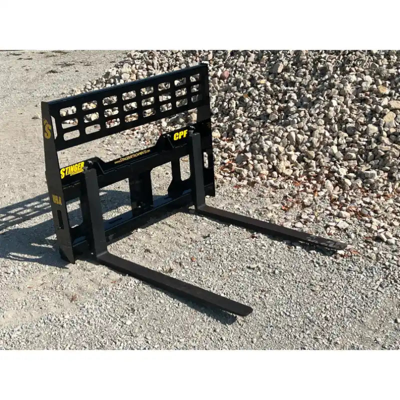 Black steel skid steer pallet fork attachment with open grid backrest and two extended fork tines on gravel surface