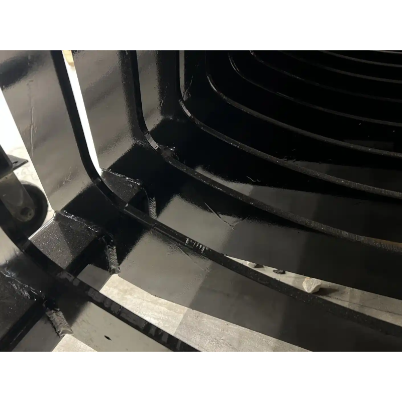 Close-up of black metal skid steer rock bucket attachment teeth welded to spaced curved tines on concrete floor