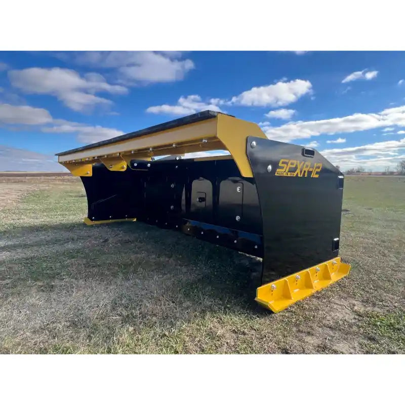 Black and yellow steel snow pusher attachment resting on grass field with clear sky and scattered clouds background