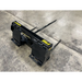Black metal skid steer attachment with pointed prongs and yellow STINNIS branding on concrete floor
