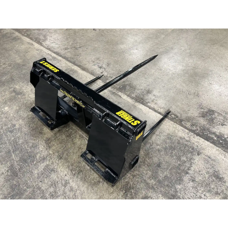Black metal skid steer attachment with pointed prongs and yellow STINNIS branding on concrete floor