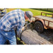 Man attaching chain to large log on Swisher ATV log skidder with knobby tires and wooden trailer nearby, gallery position 1