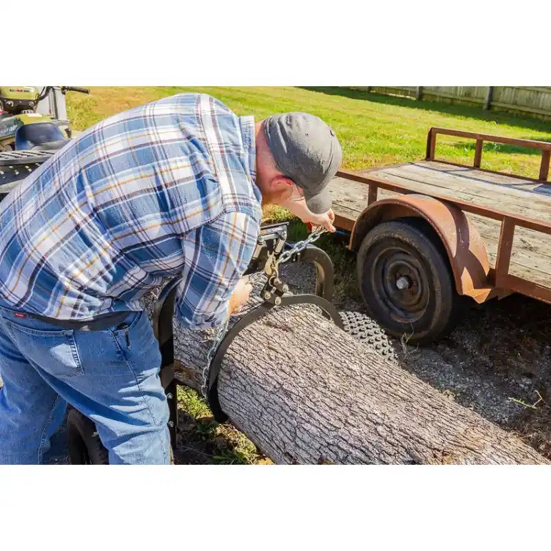 Man attaching chain to large log on Swisher ATV log skidder with knobby tires and wooden trailer nearby, gallery position 1