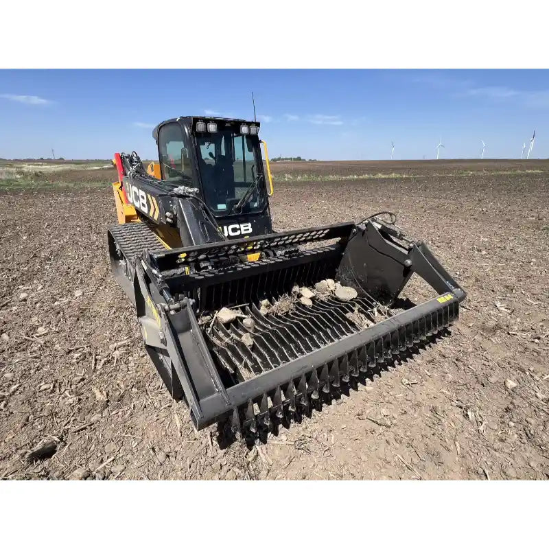 Front angled view of tracked skid steer with rock reel attachment clearing rocky soil in open field under blue sky