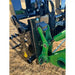 Close-up of black and green steel grapple attachment showing hydraulic connections and mounting hardware over dry grass