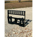 Black steel skid steer pallet fork attachment with perforated vertical backrest and mounting frame on gravel surface outdoors