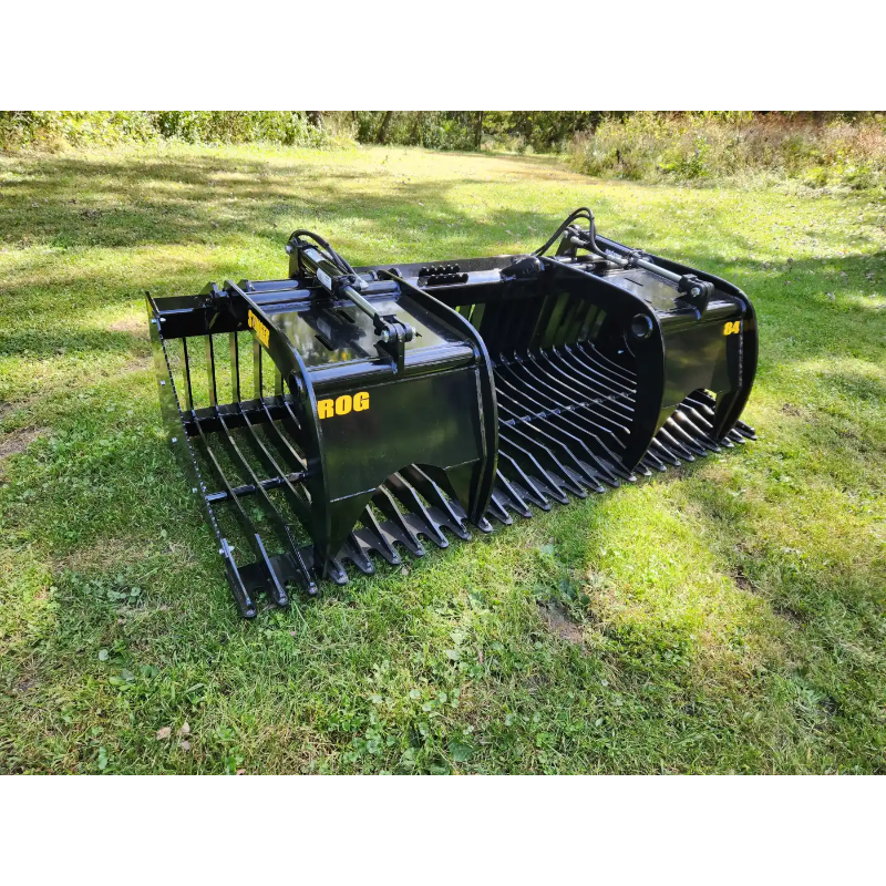 Black steel skid steer rock grapple attachment with wide spaced tines, hydraulic linkage, and reinforced side panels on grass outdoors