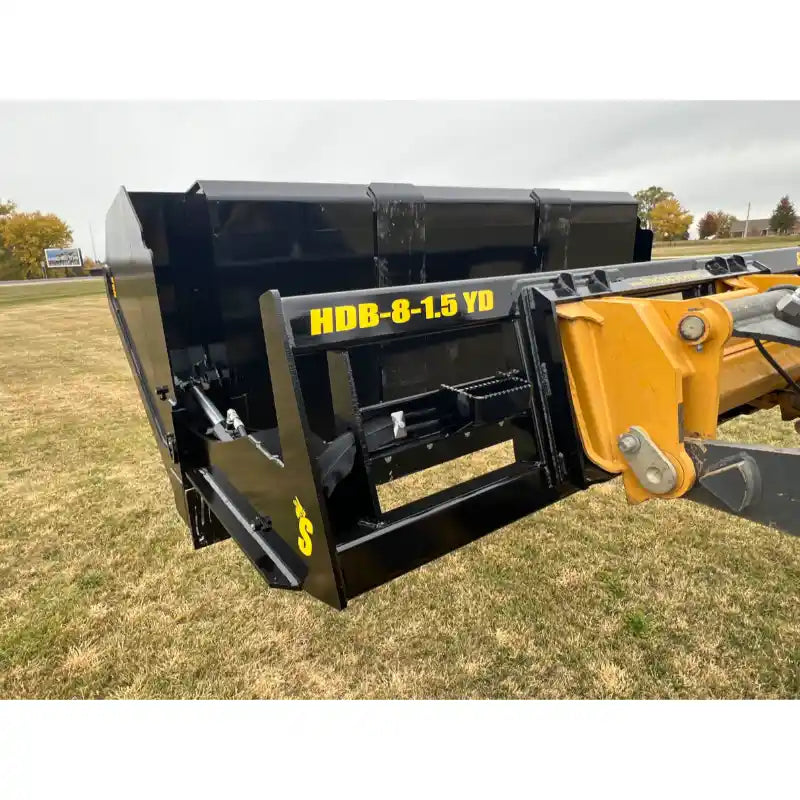 Black steel tractor hydraulic dump bucket attachment showing mounting frame and hydraulic cylinders on grass field