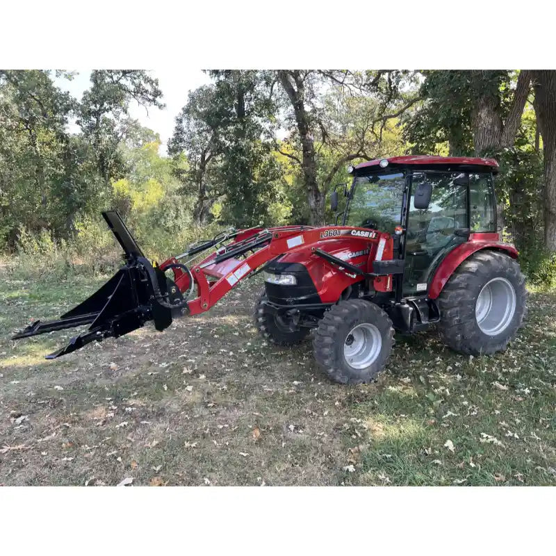 Red tractor with enclosed cab equipped with front loader and stump puller attachment on grassy woodland ground
