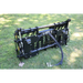 Black compact clam grapple attachment with hydraulic hoses resting on grass outdoors with sunlight and shadow patterns