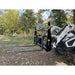Black painted steel tractor pallet fork attachment with two extended tines and perforated backrest near wooded area