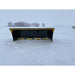 Front view of yellow and black skid steer snow pusher attachment resting in snowy open field