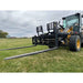 Yellow Deere skid steer loader fitted with black pallet fork attachment and extended fork tines on mowed grassy field under cloudy sky