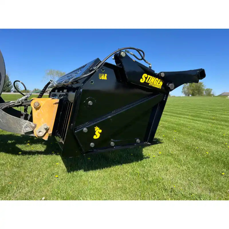 Side view of black tractor rock bucket reel attachment with yellow hitch on green grass under clear sky