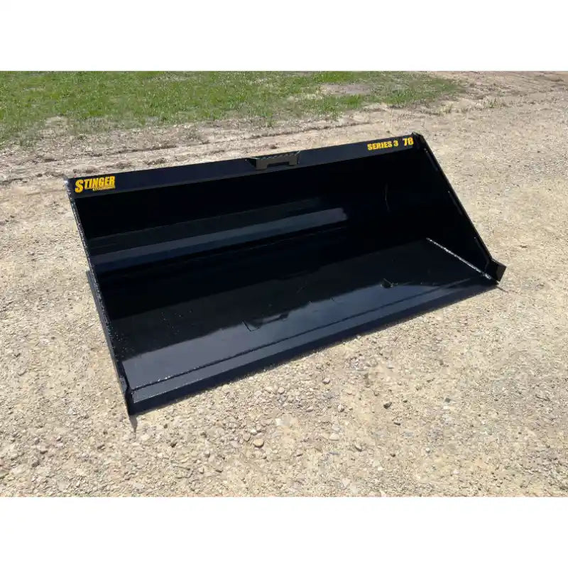 Black steel skid steer material bucket with angled sides, smooth interior, and yellow Series 3 78 Stinger labels on gravel surface
