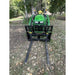 Green tractor with black steel pallet fork attachment featuring perforated grid backrest and extended fork tines on grass and dirt outdoors