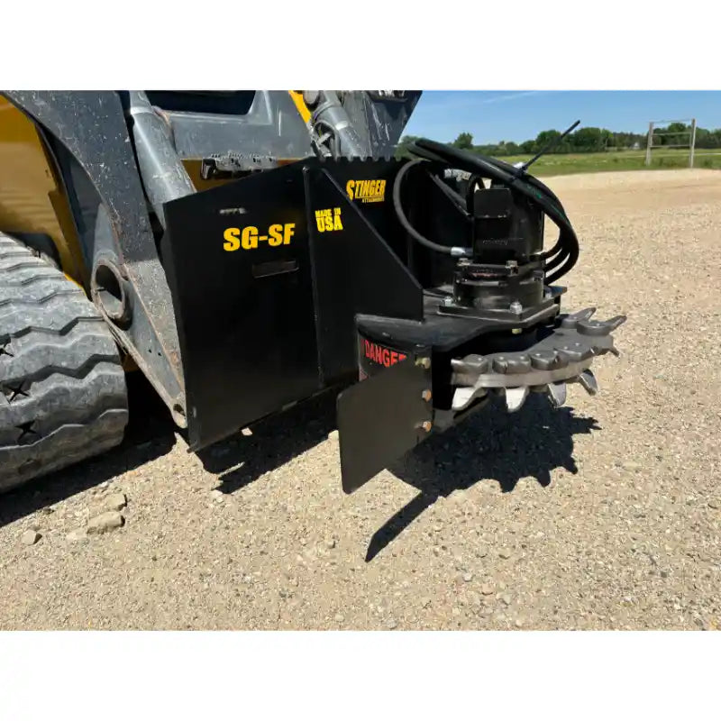 Black skid steer stump grinder attachment with cutting teeth, hydraulic hoses, and steel safety guard on dirt surface