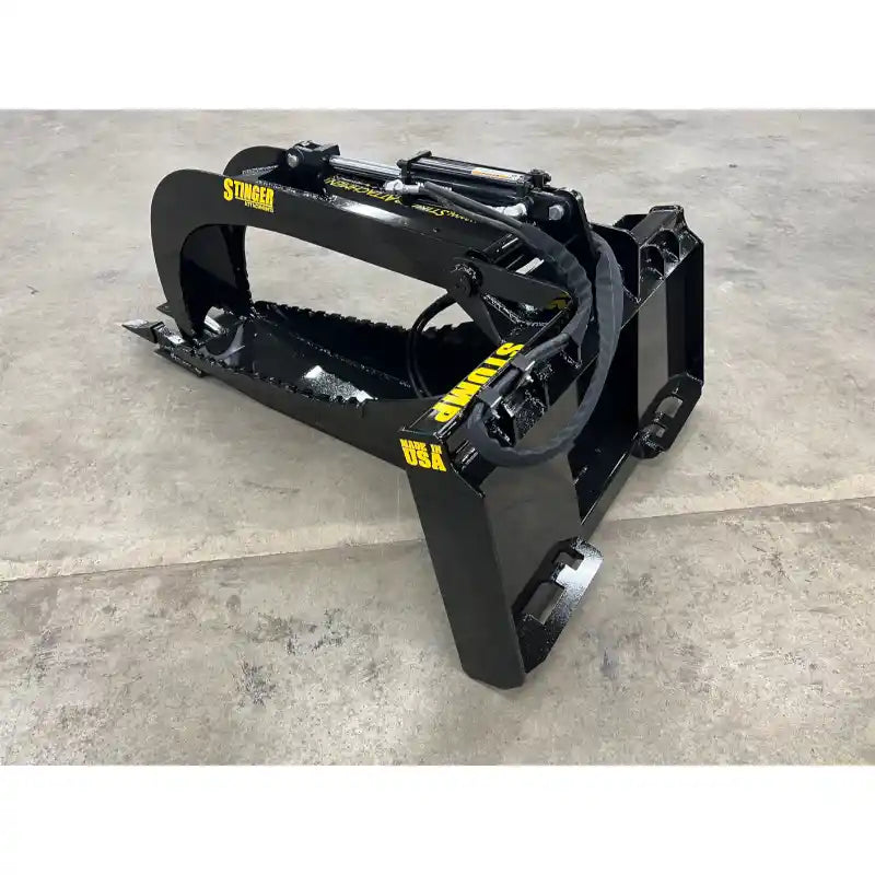 Black steel skid steer stump bucket attachment with hydraulic grapple arms and serrated edge on concrete floor